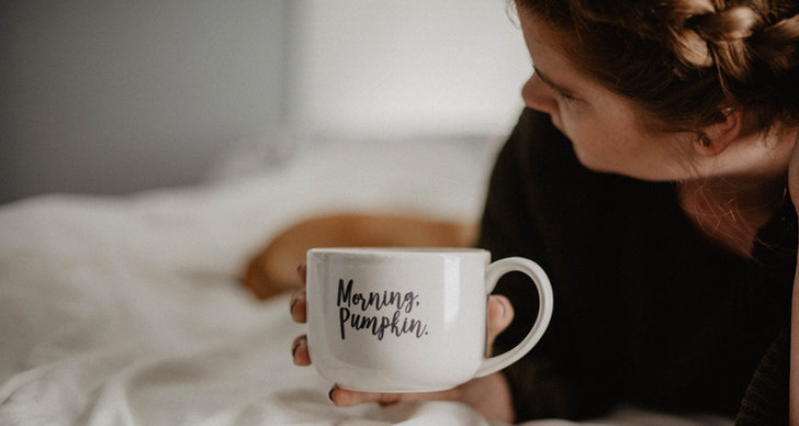 Kvinna ligger i en säng och håller i en kaffekopp