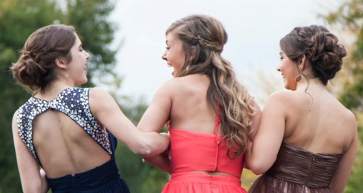 Tre festklädda tjejer håller armkrok och skrattar